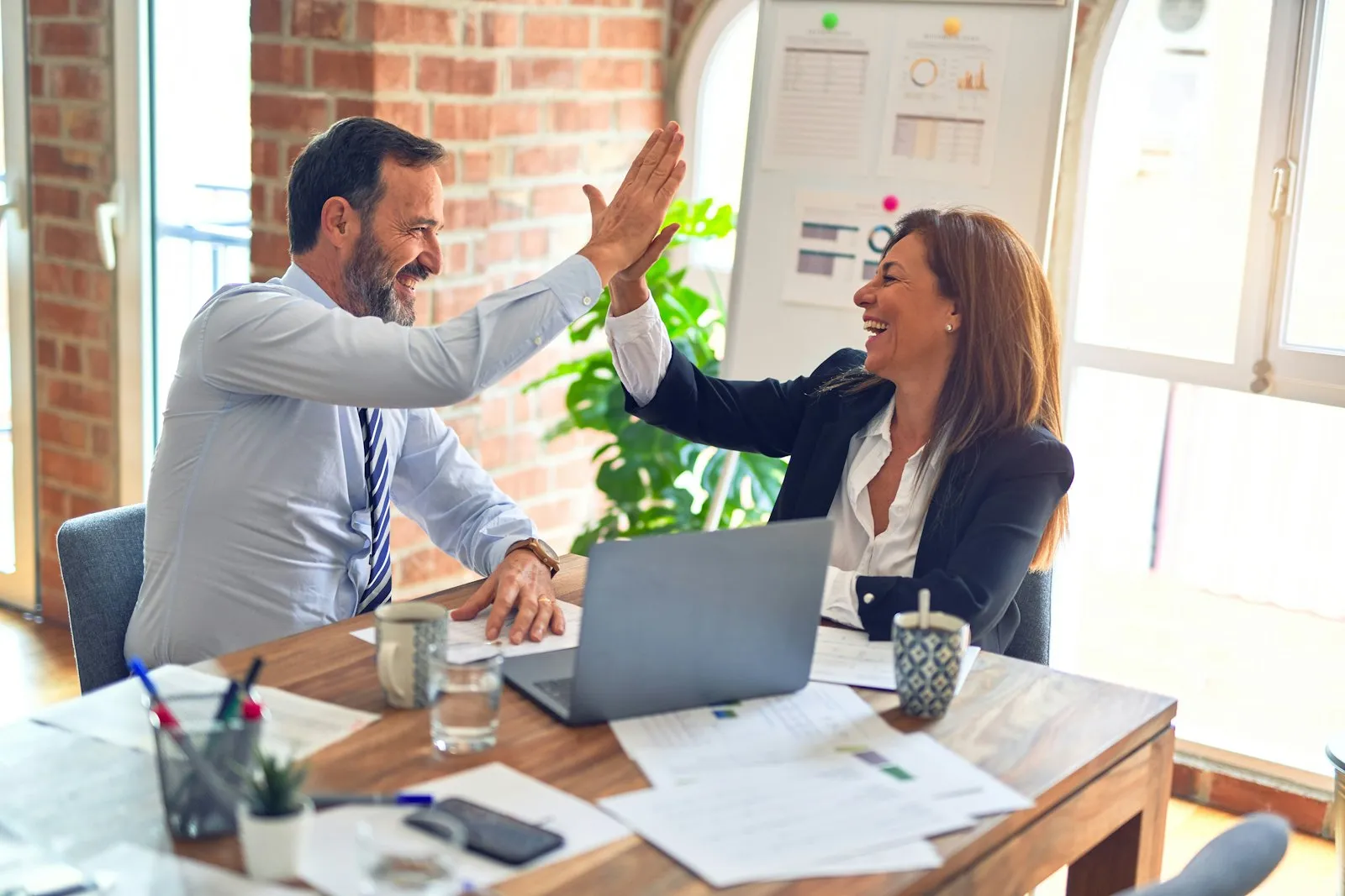 Two colleagues smiling and high-fiving at a desk in an office