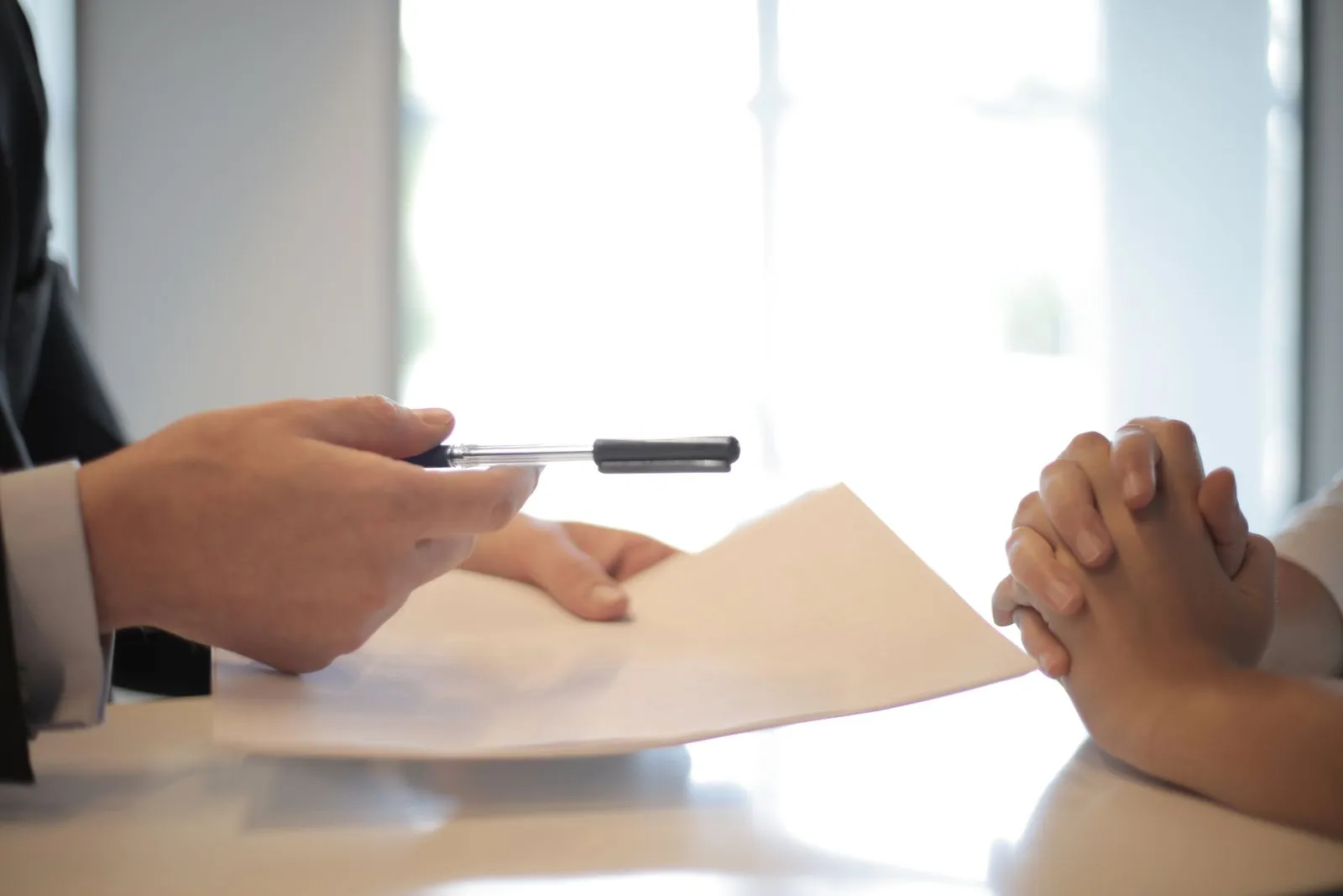 An interviewer holding out a pen over a document across a desk to a candidate